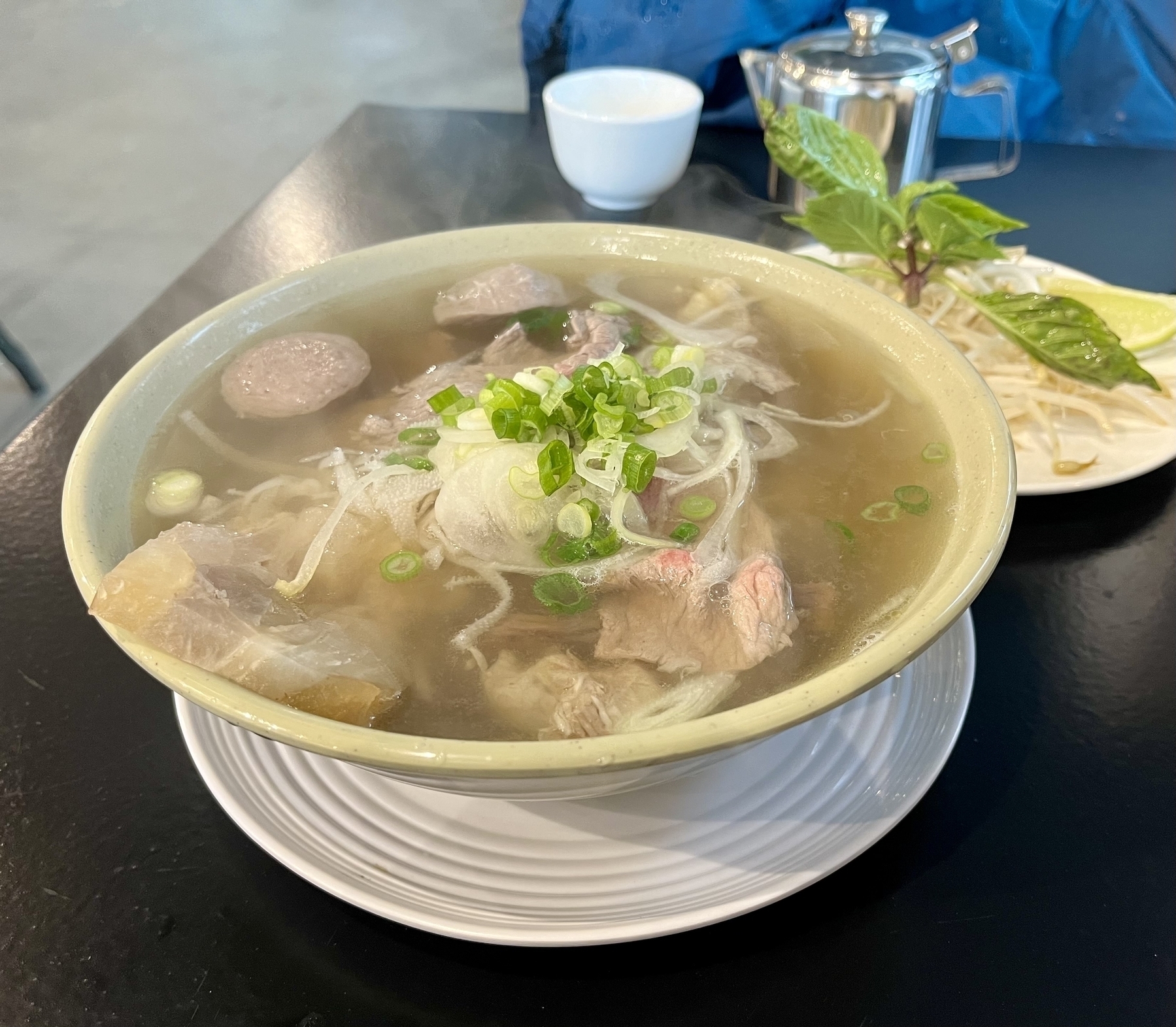 A steaming bowl of pho with all the meats. A pile of bean sprouts and fresh Thai basil. 